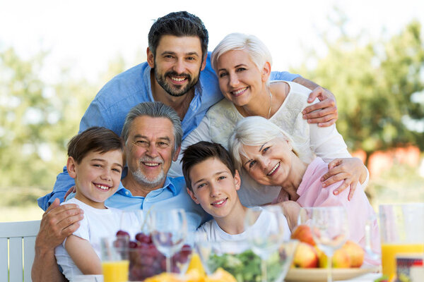 Family sitting at table outdoors, smiling