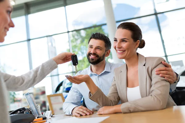 Junges Paar mit Autohändler in Autosalon — Stockfoto