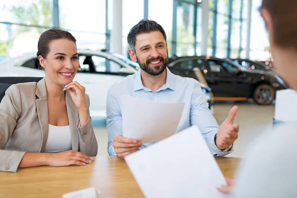 Junges Paar mit Autohändler in Autosalon — Stockfoto