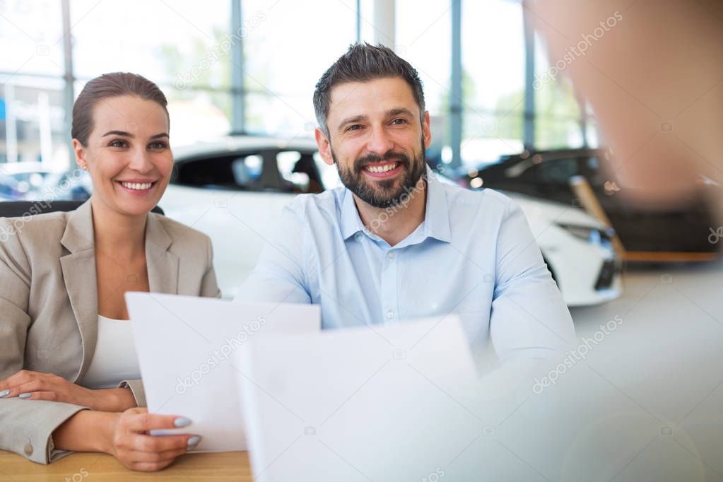 Young couple with car dealer in auto salon