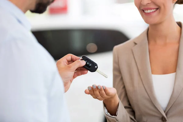 Car salesman handing car keys to woman in showroom — Stock Photo, Image