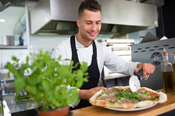 Smiling chef preparing pizza in kitchen