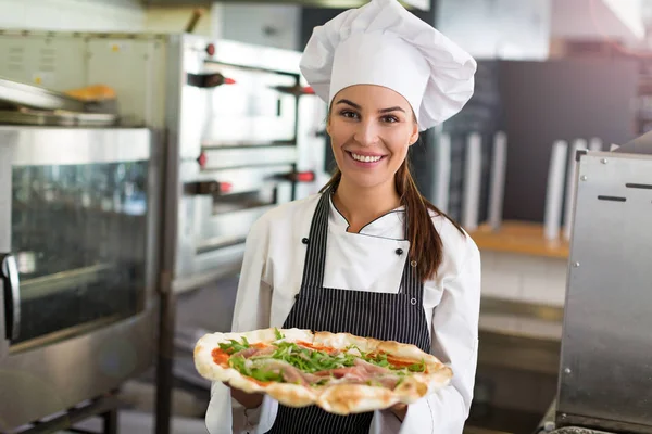 Улыбающийся шеф-повар держит свежую пиццу на кухне — стоковое фото