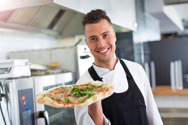 Chef souriant tenant une pizza fraîche dans la cuisine Images De Stock Libres De Droits