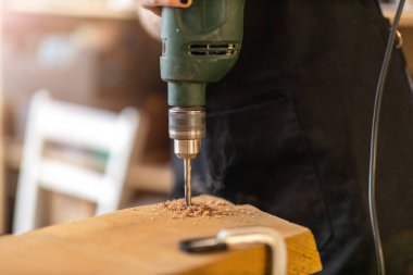 Sanayi atölyesinde elektrikli matkap kullanan genç bir kadın.