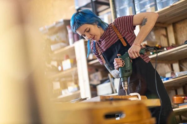 Young woman using electric drill in industrial workshop