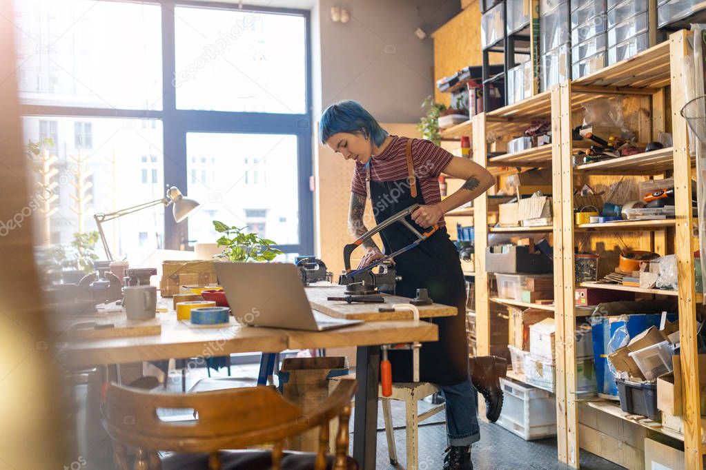 Woman cutting through block of wood using hand saw in her workshop 