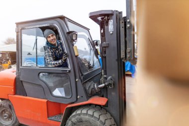 Kereste deposunda forklift kullanan genç bir erkek işçi.