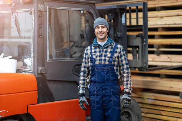 Young male worker driving forklift in lumber yard