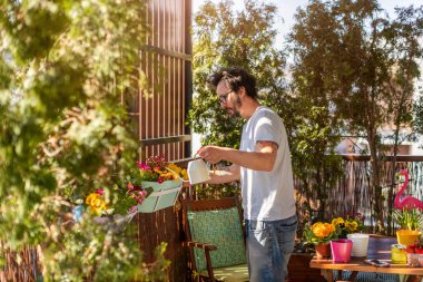 Genç adam balkonda çiçekleriyle ilgileniyor.