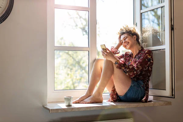 Wanita Muda Yang Duduk Ambang Jendela Dan Menggunakan Smartphone — Stok Foto