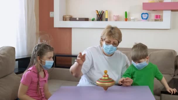 La nonna insegna ai bambini come trasformare una vecchia trottola giocattolo nella stanza. Distanziamento sociale e autoisolamento in quarantena durante la pandemia del COVID-19 . — Video Stock