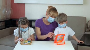 Annem tıp maskeli çocuklara odadaki faturalara güvenmeyi öğretiyor. COVID-19 salgını sırasında karantinada sosyal mesafeler ve kendini izole etme.