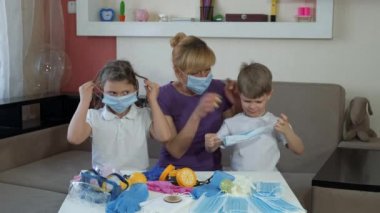 Anne çocuklara içeride tıbbi maske takmayı öğretiyor. COVID-19 salgını sırasında karantinada sosyal mesafeler ve kendini izole etme.