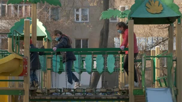 Dos niñas y un niño con máscaras médicas superan un obstáculo en el patio de recreo. El concepto de protección contra las infecciones por coronavirus covid-19 . — Vídeo de stock