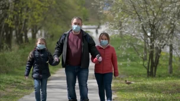 En far og to døtre i medicinske masker går i nærheden af parken. Begrebet beskyttelse fra covid-19 coronavirus infektioner . – Stock-video