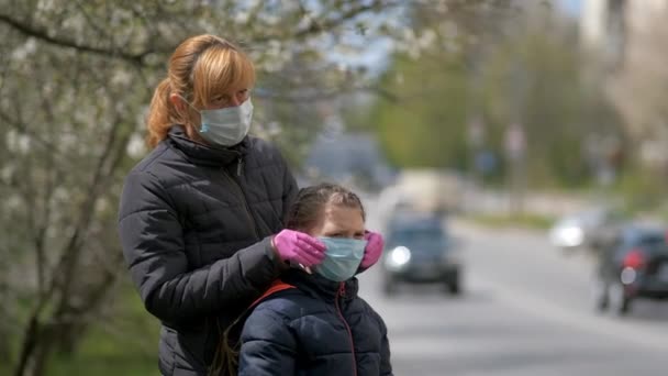 Mère ajuste le masque médical de ses filles dans la rue d'une ville européenne. Le concept de protection contre l'infection par le coronavirus COVID-19 . — Video