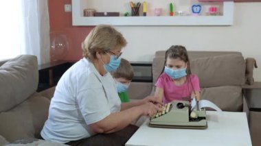 Büyükannem çocuklara odada daktilo kullanmayı öğretiyor. COVID-19 salgını sırasında karantinada sosyal mesafeler ve kendini izole etme.