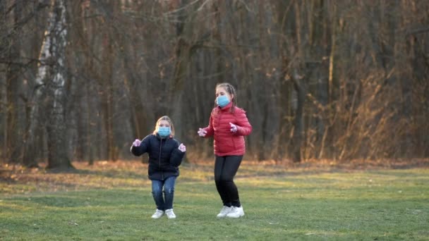 Twee Meisjes Met Medische Maskers Springen Een Lentepark Langzame Beweging — Stockvideo