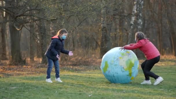两个戴着口罩的女孩在春天公园里与一个巨大的充气球行星地球玩耍 Coronavirus Infections Covid 19的保护概念 — 图库视频影像