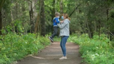 Tıbbi maskeli ve lastik eldivenli anne ve oğul bahar parkında dönüyorlar. Covid-19 Coronavirus enfeksiyonundan korunma kavramı.