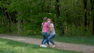 Tıbbi maskeli ve lastik eldivenli anne ve kızı bahar parkında dönüyorlar. Ağır çekim. Covid-19 Coronavirus enfeksiyonundan korunma kavramı.