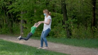 Tıbbi maskeli ve lastik eldivenli anne ve oğul bahar parkında dönüyorlar. Ağır çekim. Covid-19 Coronavirus enfeksiyonundan korunma kavramı.