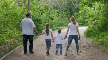 Aile: Baba, anne, oğul ve kız tıbbi maskeler, beyaz tişörtler ve lastik eldivenlerle parkta yürüyorlar. Dikiz aynası. Covid-19 koronavirüs enfeksiyonlarından korunma kavramı.