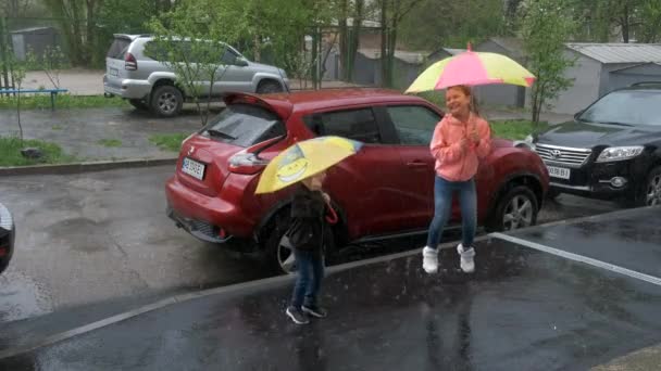 기쁨에 소녀와 소년은 속에서 우산을 가지고 근처에 차들의 배경에 즐겁게 — 비디오
