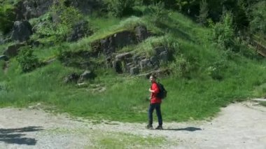 Kırmızı ceketli ve siyah sırt çantalı genç bir adam bir yaz günü dağlarda seyahat ediyor.. 