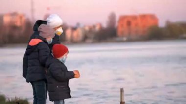 Tıbbi maskeli anne, oğul ve kız göldeki parkta ördekleri besliyor. Bir salgın durumunda hayvanlara yardım kavramı.