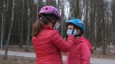 Büyük kız kardeş parkta bisiklet sürmeye gitmeden önce küçük kız için bir tıbbi maske takar. Covid-19 koronavirüs enfeksiyonlarından korunma kavramı.