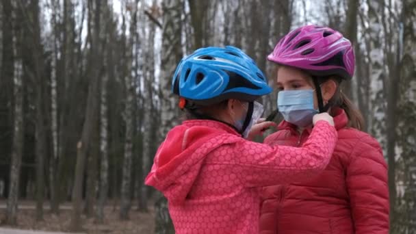 姉は公園で自転車に乗る前に若い人のための医療マスクをつけています Covid 19コロナウイルス感染からの保護の概念 — ストック動画
