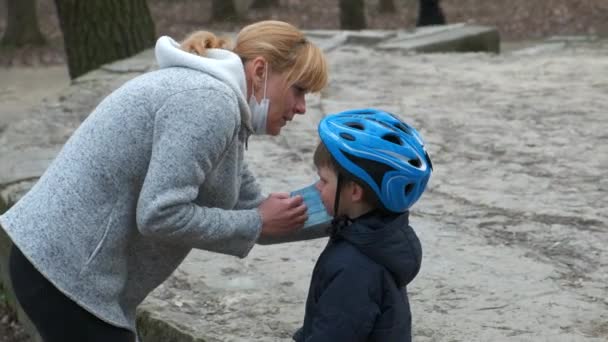 母は公園でサイクリングする前に息子のための医療マスクをつけています Covid 19コロナウイルス感染からの保護の概念 — ストック動画