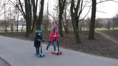 Küçük bir oğlan ve kız parkta maske takıp scooter 'a biniyorlar. Covid-19 koronavirüs enfeksiyonlarından korunma kavramı.