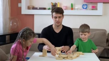 Ağabeyi çocuklarla ahşap oyuncaklarla oynuyor. Bloklardan kuleler inşa ediyorlar. COVID-19 salgını sırasında karantinada sosyal mesafeler ve kendini izole etme.