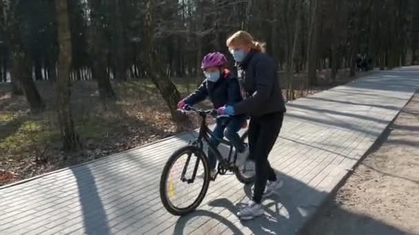 妈妈在城市公园教她的女儿骑自行车 他们戴着防护头盔和医疗面具 Covid 19型大肠病毒感染防护概念 — 图库视频影像