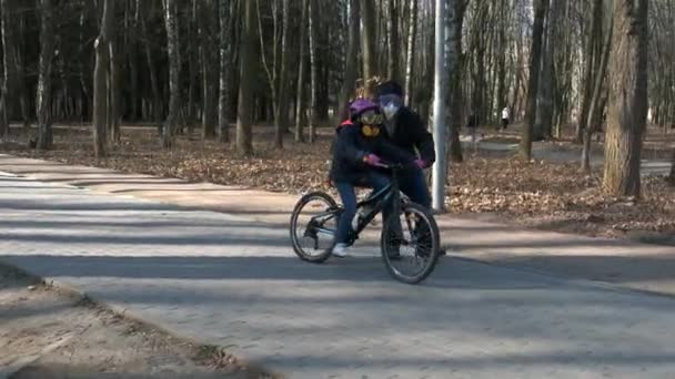 父親は娘に都市公園で自転車に乗るように教える 防護ヘルメットとマスクを着用しています Covid 19コロノウイルス感染からの保護の概念 — ストック動画