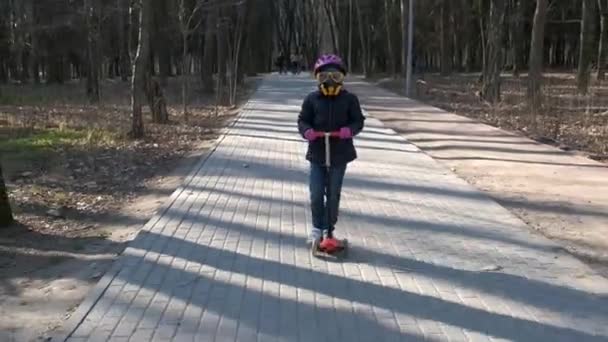 Una Bambina Cavalca Attraverso Parco Primavera Uno Scooter Con Casco — Video Stock