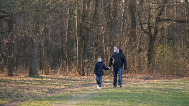 父と娘は医療マスクで春の公園を歩く コロナウイルス感染に対する保護の概念 Covid — ストック動画