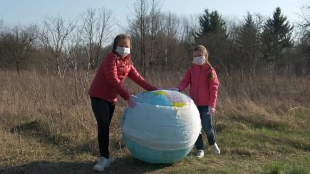 两个小女孩在一个膨胀的球状行星地球上戴上了纱布面具 Coronavirus Infections Covid 19的保护概念 — 图库视频影像