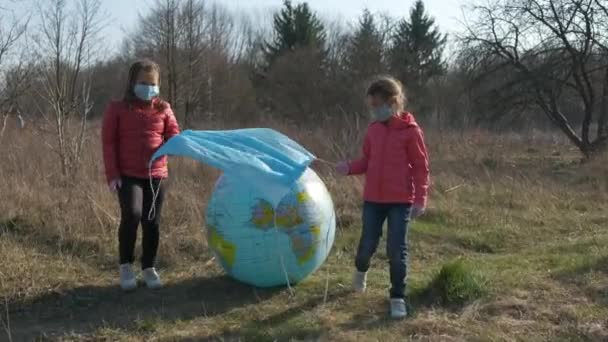 2人の小さな女の子が青い医療用マスクを膨脹可能な球惑星地球に置きました コロナウイルス感染に対する保護の概念 Covid — ストック動画