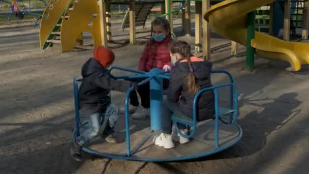Troje Dzieci Maskach Medycznych Jeździ Karuzeli Placu Zabaw Koncepcja Ochrony — Wideo stockowe