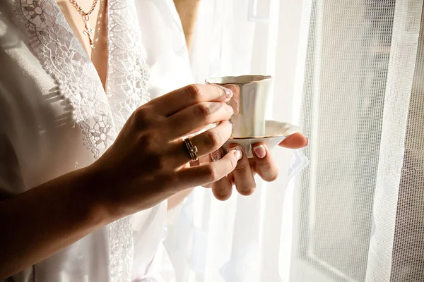 Evdeki pencerenin yanında sıcak kahve fincanı tutan bir kadının ellerini yakın plan..