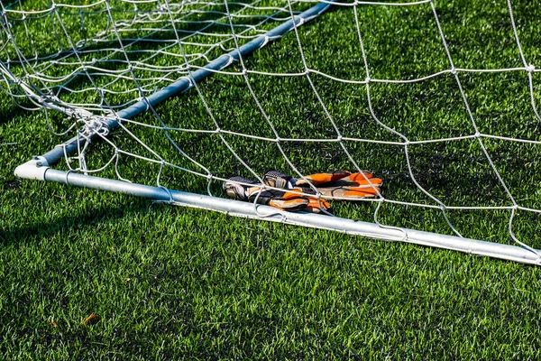 ゴールキーパーの手袋はサッカーのゴール近くの草の上にあります — ストック写真