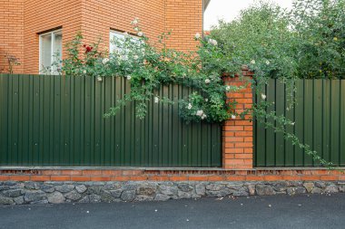 Önünde çimen, arkasında ağaçlar olan yeşil kıvrımlı metal levha panellerinden yapılmıştır.