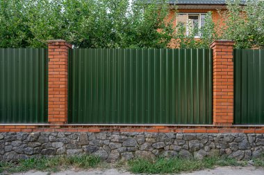 Önünde çimen, arkasında ağaçlar olan yeşil kıvrımlı metal levha panellerinden yapılmıştır.