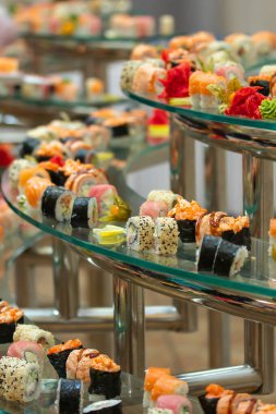 Cam büfede bir sürü suşi rulosu var. Doğu dekorlu geleneksel Japon yemekleri masasında. yemek servisi..
