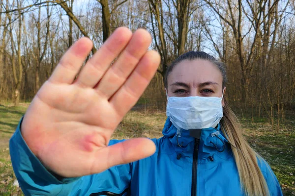 Korunmak için maske takan ve Corona virüsünü durdurmak için el hareketi yapan bir kız.