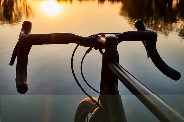 Rower w pobliżu jeziora, kierownica nad wodą na tle zachodzącego słońca, rower żwirowy z bliska — Zdjęcie stockowe